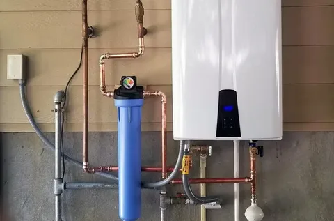 A white wall-mounted tankless water heater and blue water filtration system connected with copper piping, showcasing a modern water heater replacement solution for improved home efficiency.