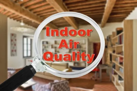 A magnifying glass held in the foreground focuses on the red text improve Indoor Air Quality, with a blurred living room interior visible in the background.