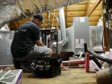 Technician inspecting HVAC equipment and ductwork in an attic while evaluating furnace repair vs replacement options for home heating performance.